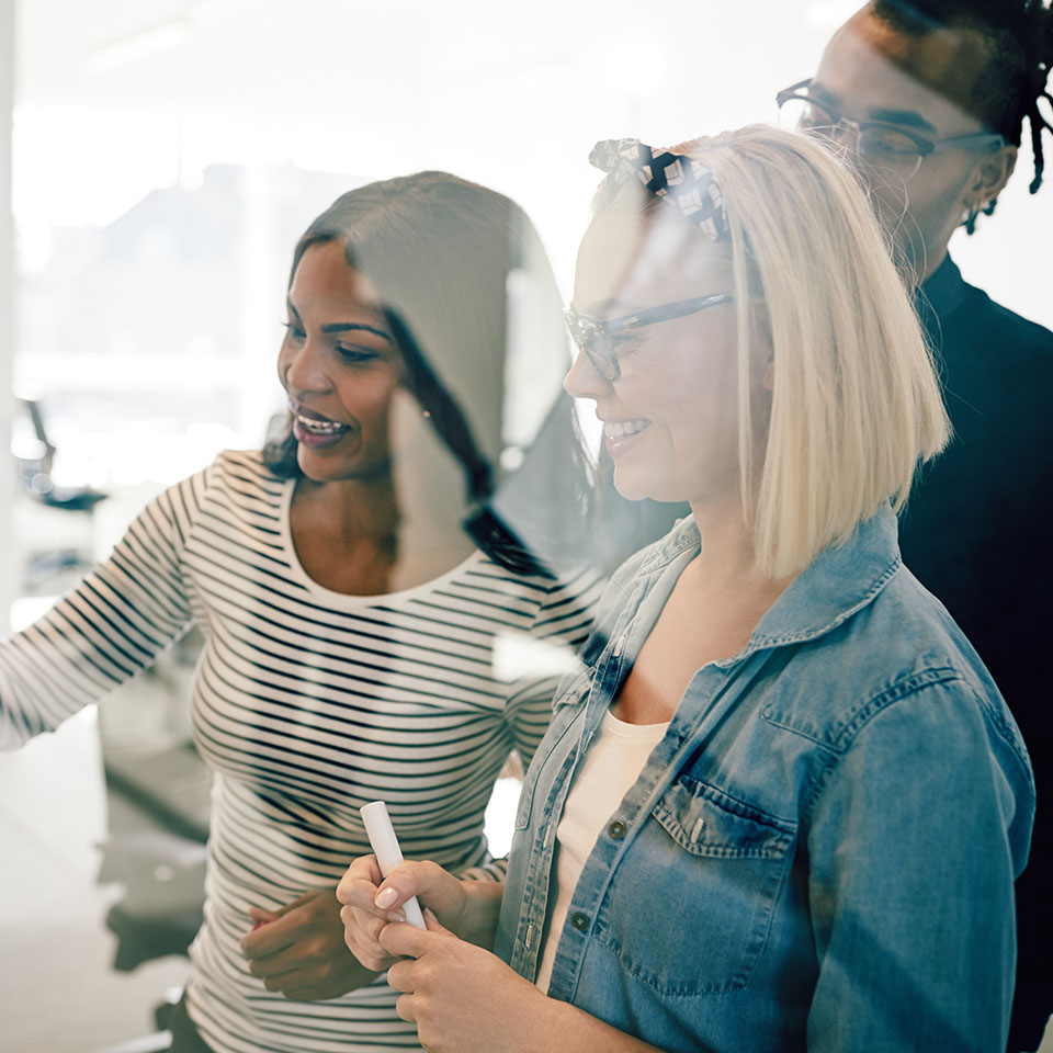 Group of diverse young work colleagues smiling while brainstorming together with sticky notes on the glass wall of a modern office