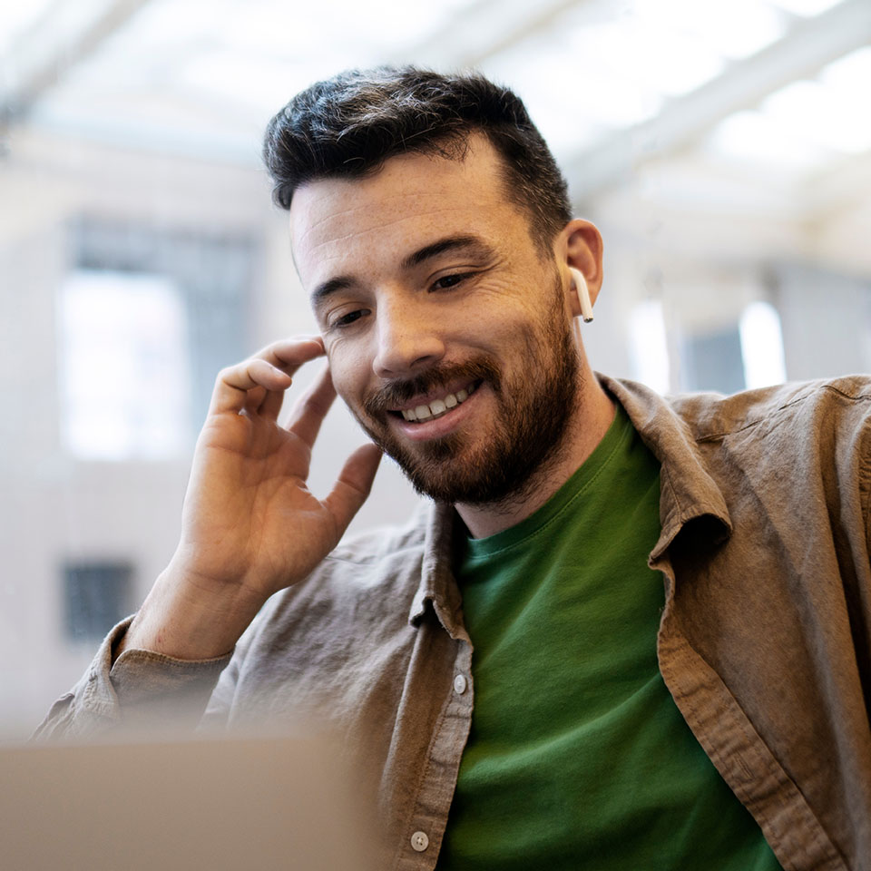 Attractive, smiling man in wireless earphones having video conference, using laptop. Successful businessman has online communication with partner. Concept of online education, remote work