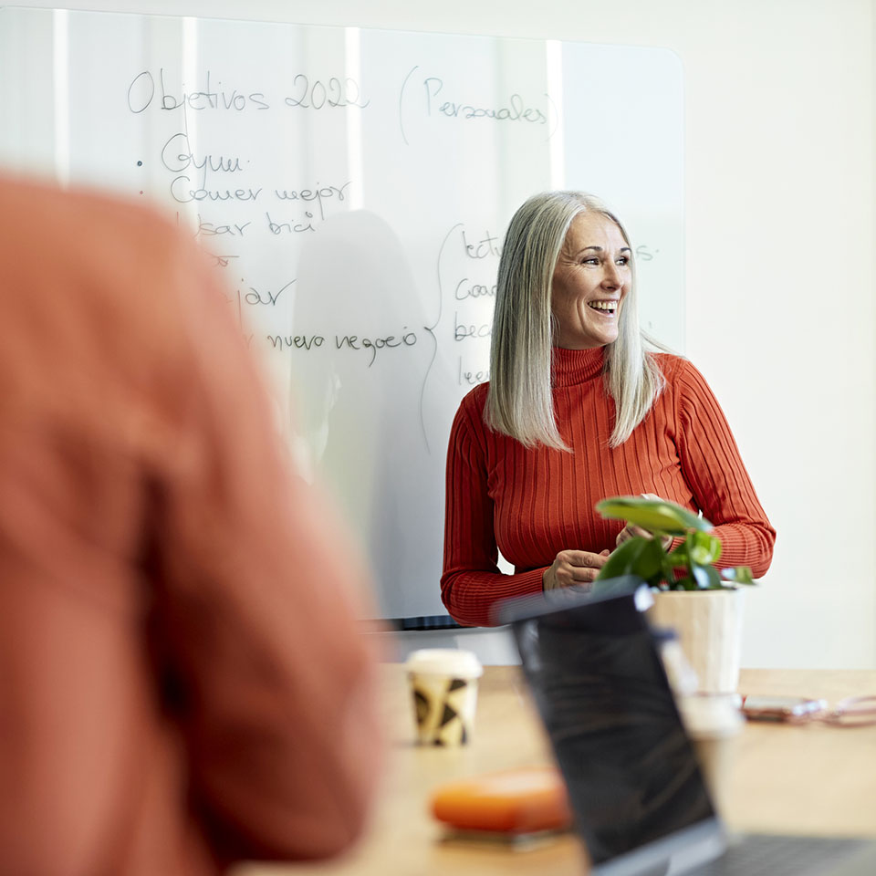 Personal perspective of mid 50s executive smiling and looking away as she receives applause from colleagues for her ideas at informal meeting.